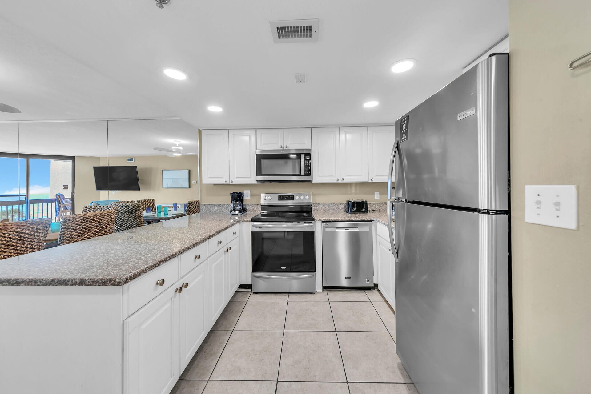 A modern kitchen with white cabinets, stainless steel appliances, a granite countertop, and a view of the ocean through a sliding glass door.