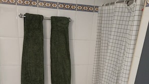A small bathroom with a toilet, two towels, a shower curtain, and a toilet paper holder. - H. Central Funchal (Madeira)