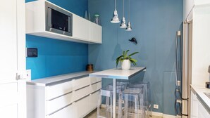 Una cocina moderna con una pared azul decorativa, armarios blancos, un microondas y una pequeña planta en maceta.
