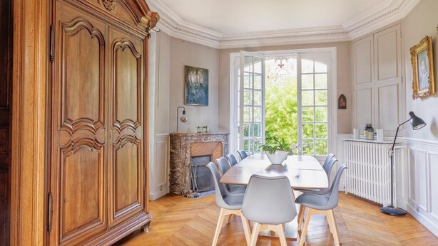 Un comedor con piso de madera en patrón de espiga, una mesa blanca y sillas grises.