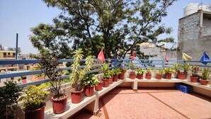 A rooftop terrace with potted plants, a blue railing, and a view of the cityscape. - Harish Guest House -Railway Station Road (Chandigarh)