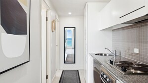 A narrow kitchen with a view to the sea, a sink, stove, and a small rug. - Belle Escapes - Beachfront Balcony Glenelg (Glenelg)