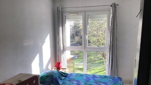 Quarto pequeno com uma cama, uma escrivaninha e uma janela com cortinas.