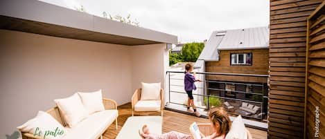 Un espace de vie extérieur moderne, avec des meubles en osier, une table blanche et un balcon doté d’une balustrade.