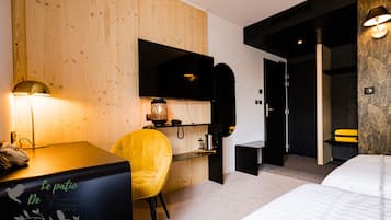 A modern hotel room with a wooden wall, a desk with a lamp, a yellow chair, a bed, and a TV mounted on the wall.