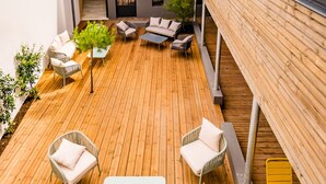 Una terraza de madera con mobiliario exterior, incluyendo un sofá y sillas, y una mesa amarilla.