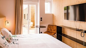 Habitación de hotel con cama, televisor, una pequeña mesa, una silla y balcón con paredes de madera y vistas al exterior.
