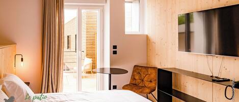 A hotel room with a bed, a TV, a small table, a chair, and a balcony with wooden walls and a view of the outside.