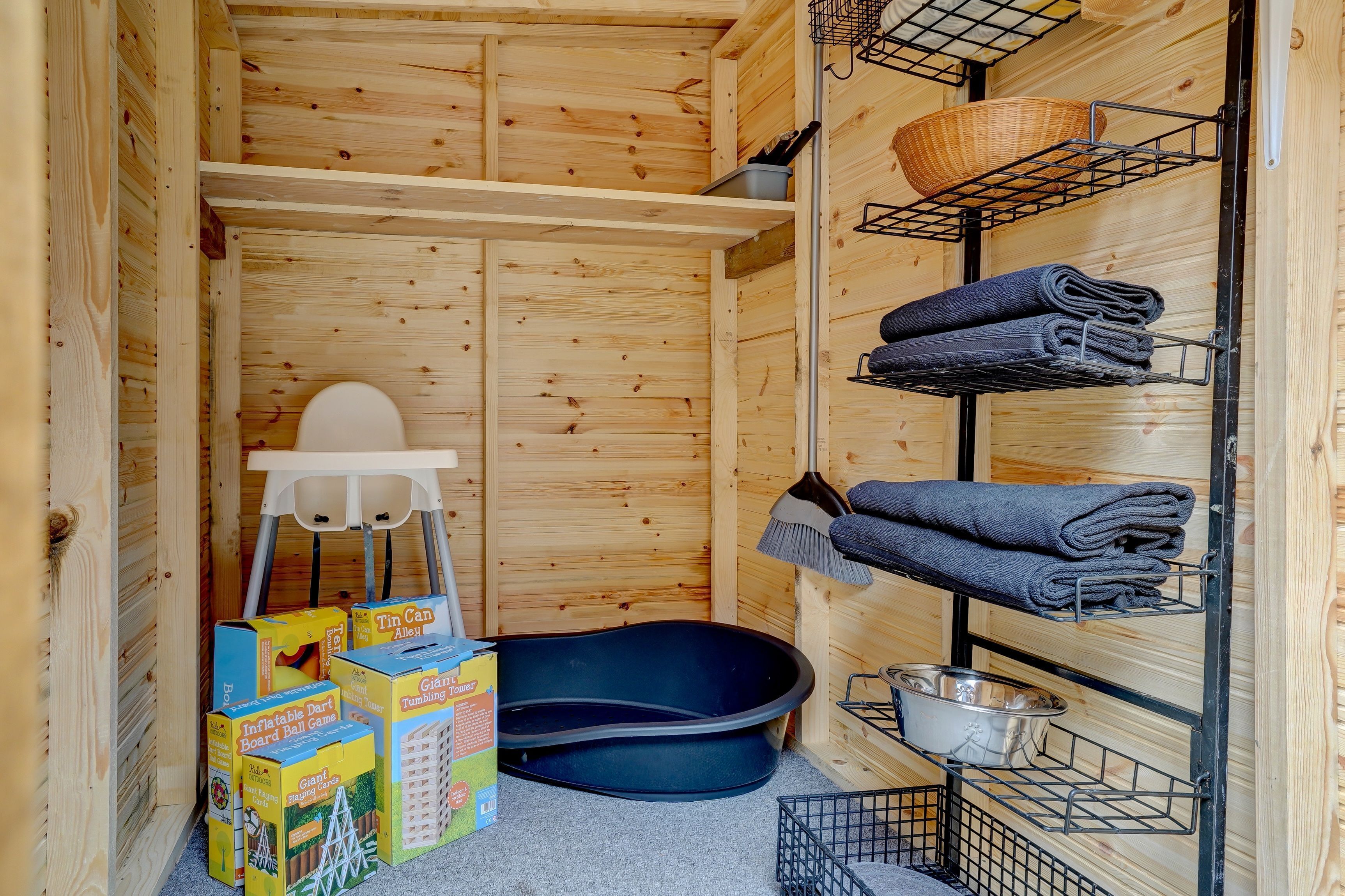 Interior de una cabaña de madera con una bañera negra, repisas con toallas dobladas, una silla blanca y cajas de almacenamiento.