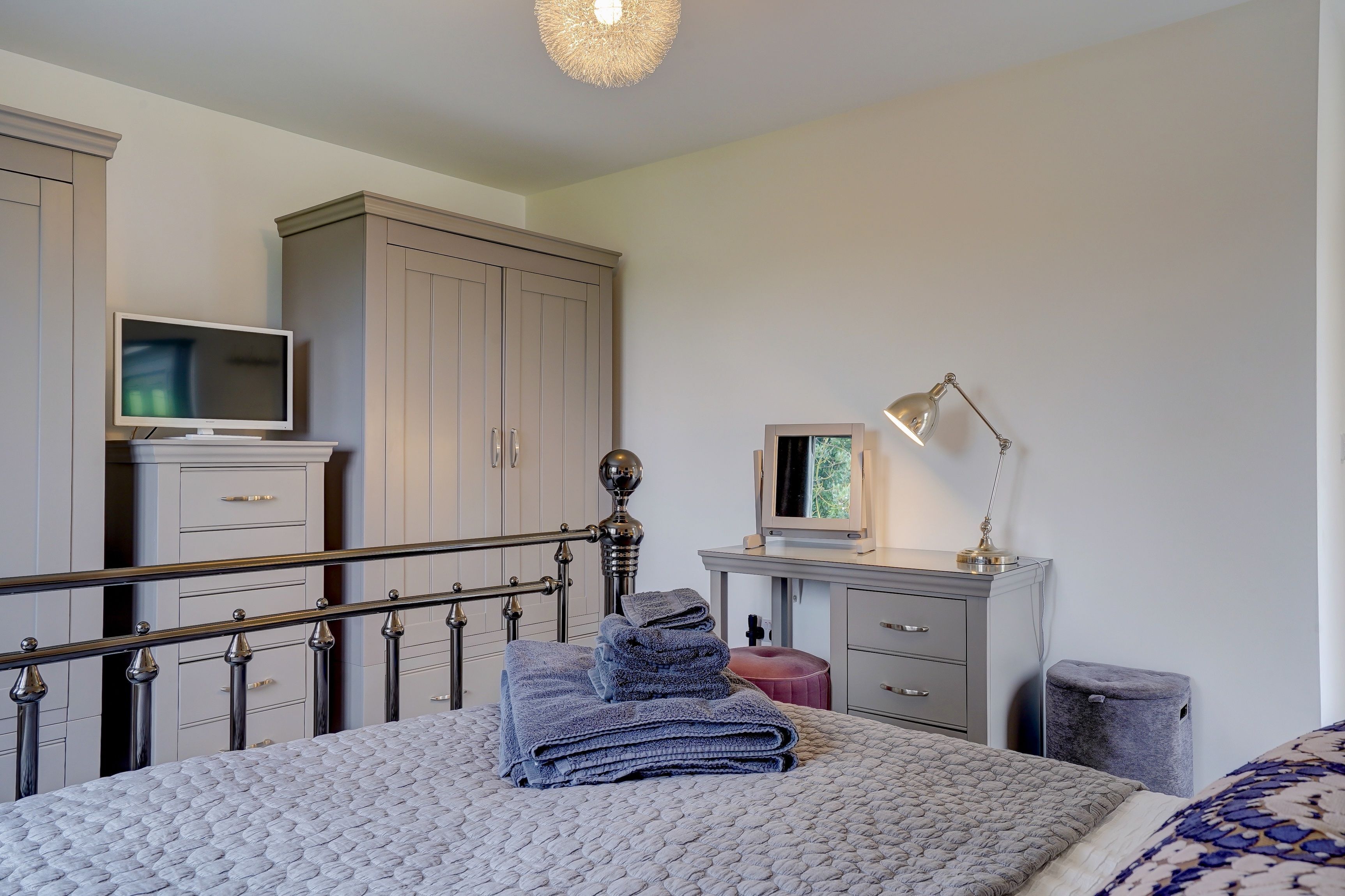 A bedroom with a bed, a TV, a desk, and a wardrobe.