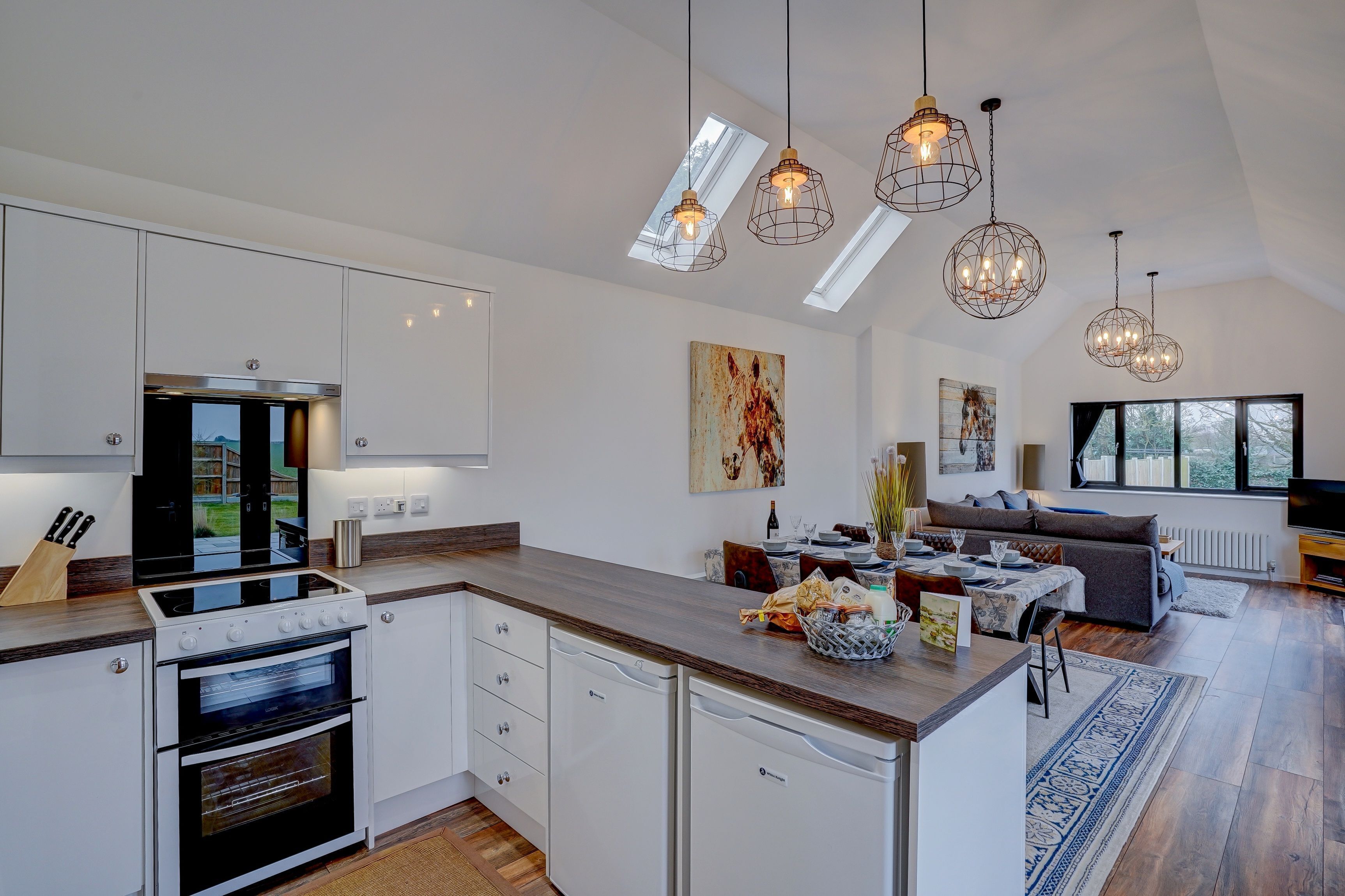 Une cuisine moderne avec des meubles blancs, un four encastré et un coin repas comprenant un canapé et une table.