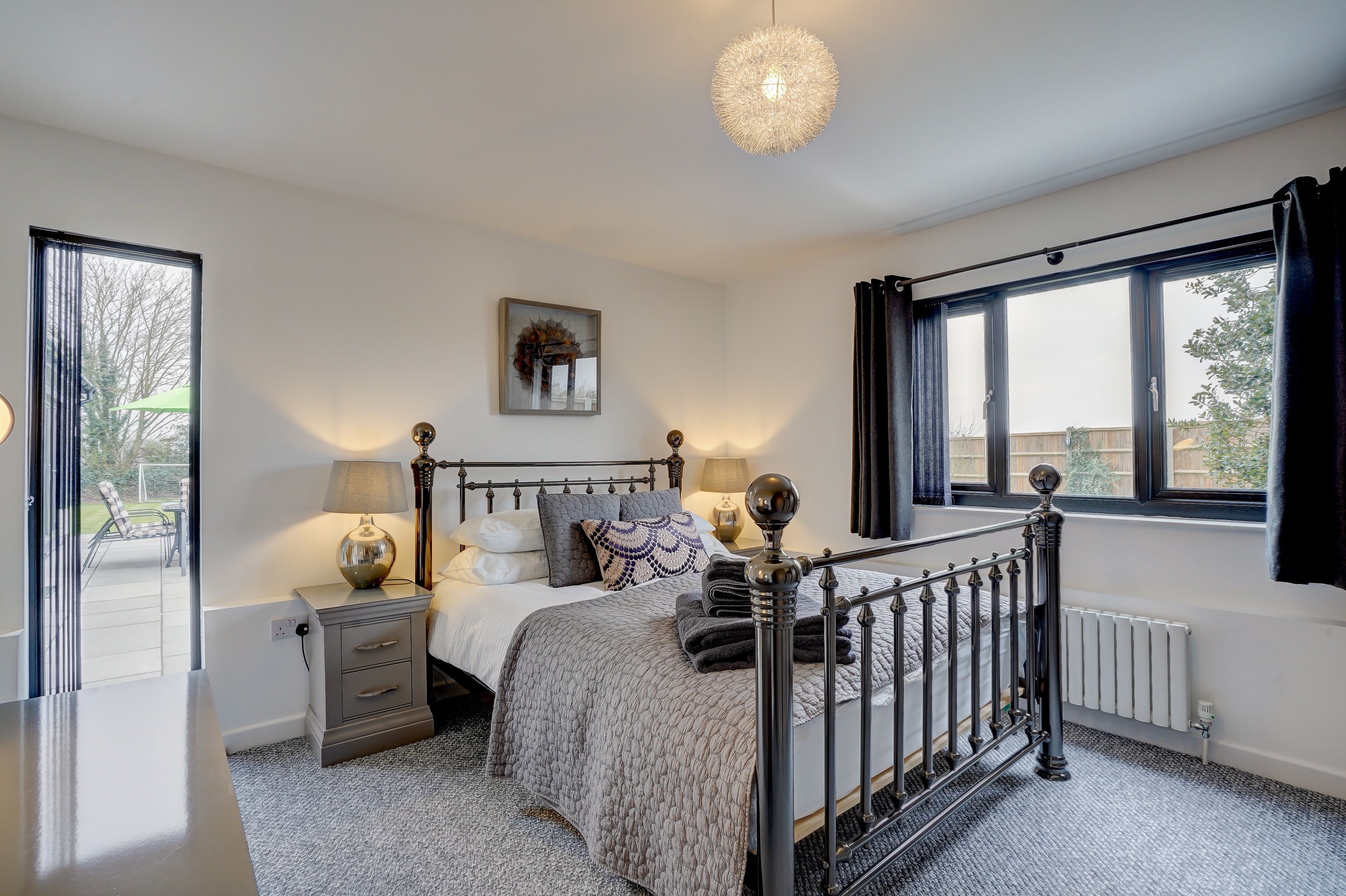 A bedroom with a bed, bedside tables, a lamp, a radiator, and a window with curtains.