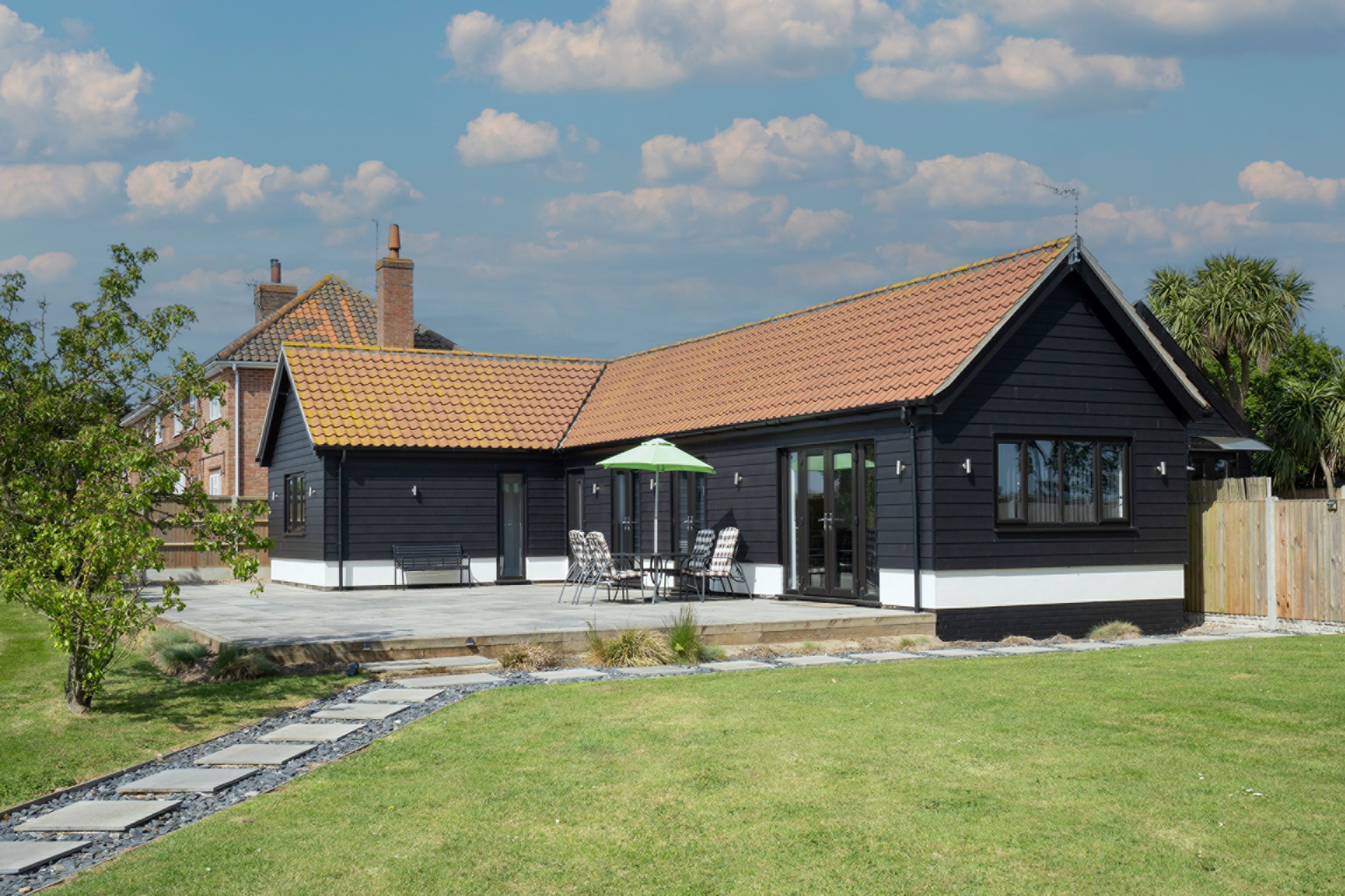 Une maison moderne avec un toit en pente, une terrasse dotée de mobilier d’extérieur et une pelouse bien entretenue.