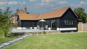 Une maison moderne avec un toit en pente, une terrasse dotée de mobilier d’extérieur et une pelouse bien entretenue.