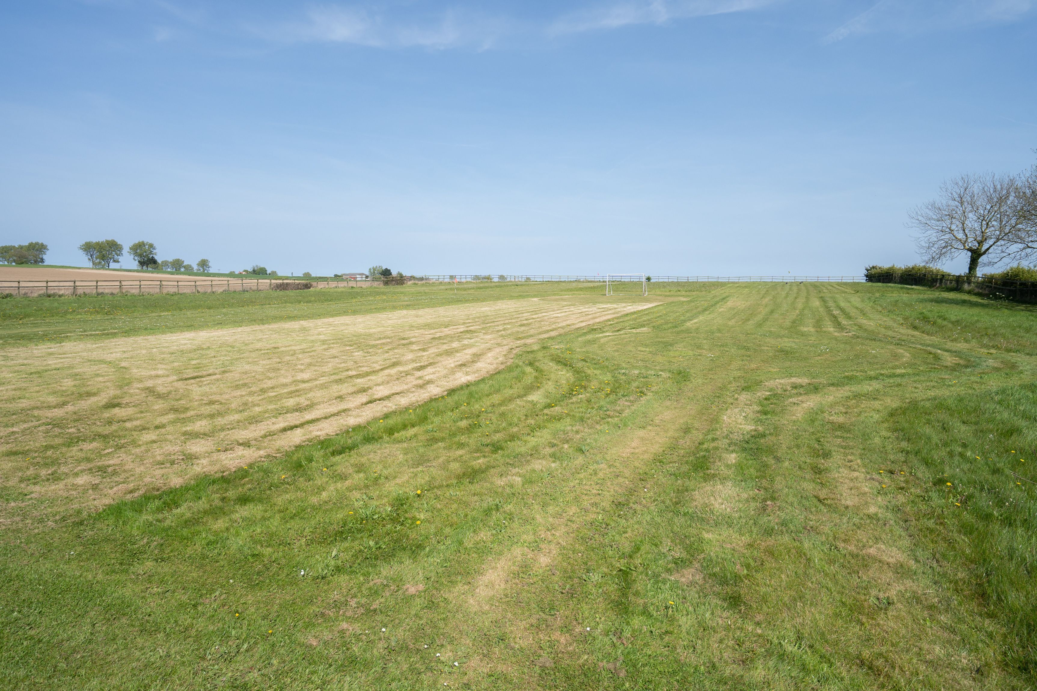Un campo cubierto de césped con un arco de fútbol y una cerca a lo lejos.
