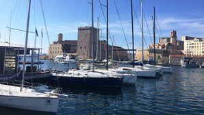 A marina with multiple sailboats docked, a historic building with a tower, and a clear blue sky. - Appartement en Étage Élévé Avec Terrasses (Marseille)