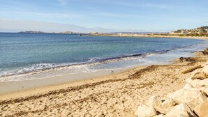 A coastal beach with clear blue waters, rocky shoreline, and distant buildings. - Appartement en Étage Élévé Avec Terrasses (Marseille)