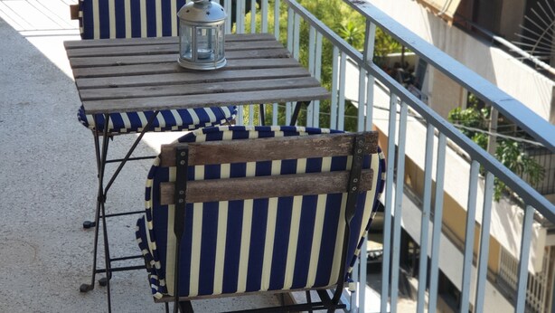 Un balcon avec deux chaises à rayures et une petite table, une lanterne et une rambarde.