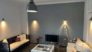 Un salon moderne comprenant un canapé, une table basse, un téléviseur et des luminaires fixés au mur.