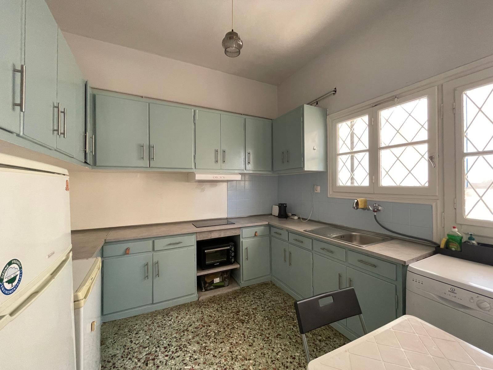 Une cuisine avec des meubles de couleur bleu clair, un réfrigérateur blanc, un four à micro-ondes et une fenêtre avec des vitres à motifs losangés.
