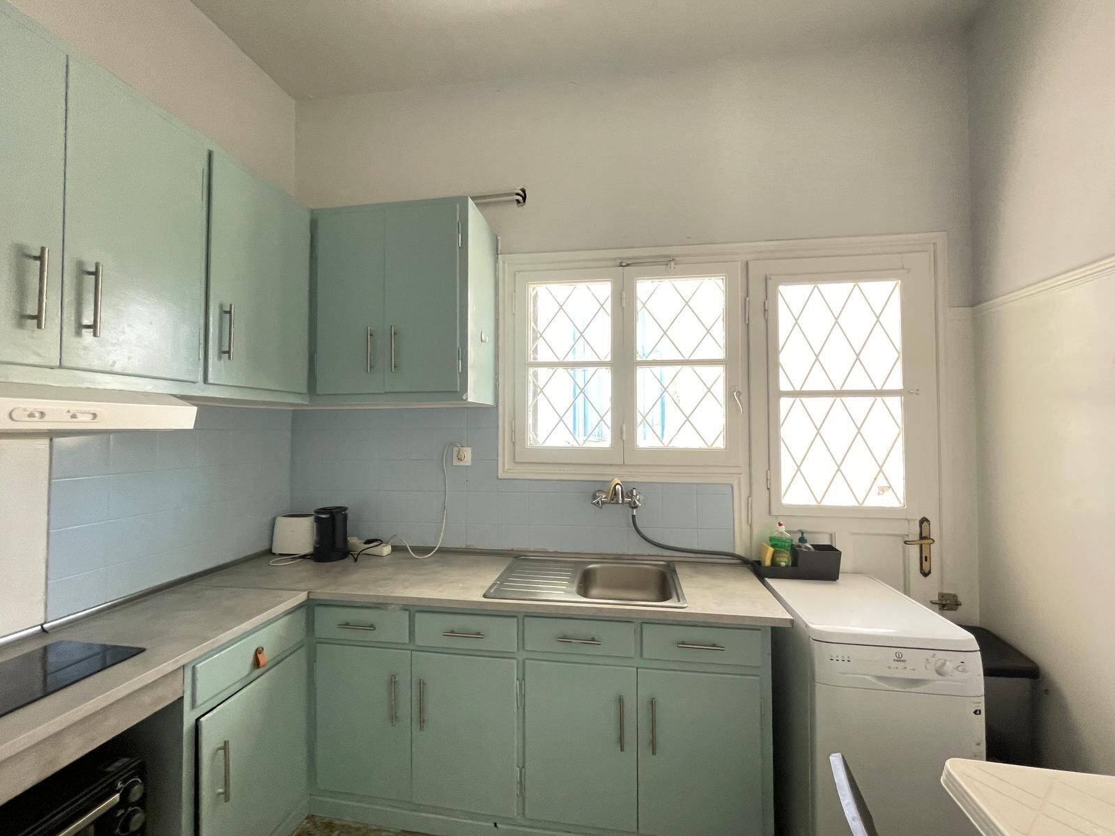 Une cuisine compacte avec des meubles de couleur turquoise, un four encastré et un lave-vaisselle.