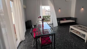 Un salon moderne avec une table à manger en verre, des chaises à coussins rouges, un canapé noir et une table basse blanche.