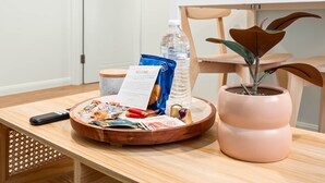 Une table en bois, sur laquelle on a posé une carte de bienvenue, une bouteille d’eau, des en-cas et une plante en pot.
