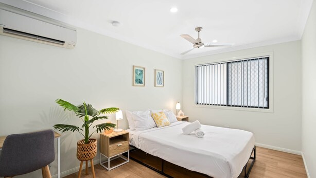 Une chambre à coucher avec un lit, un bureau, une chaise, une plante en pot et un ventilateur de plafond.