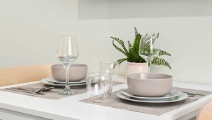 Une table à manger dressée avec deux bols, deux verres à vin et une fougère en pot.