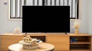 Uma sala de estar moderna com televisão de tela plana, móveis de madeira, um vaso e uma tigela decorativa.