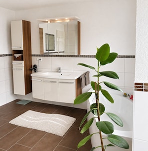 Casa de banho com lavatório, espelho, armários e uma planta.