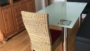 A dining area with a glass-top table, wicker chair, and a wooden cabinet with glass doors.