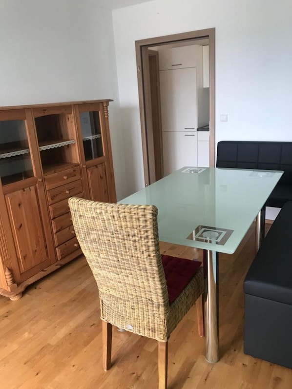 Uma sala de jantar com mesa de vidro, cadeira de vime e um armário de madeira com portas de vidro.