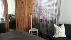 A bedroom with a bed, a sofa, a wardrobe, and a window with curtains.