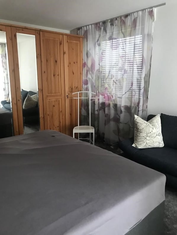 Ein Schlafzimmer mit einem Bett, einer Couch, einem Kleiderschrank und einem Fenster mit Vorhängen.