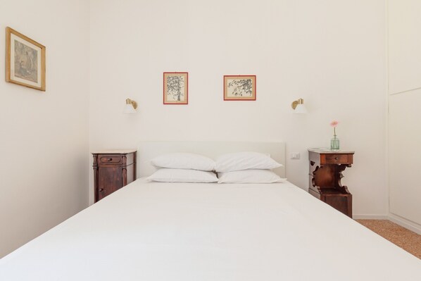 Un dormitorio con una cama grande, dos mesitas de noche y una mesita de noche con un florero.