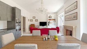 A modern kitchen with built-in appliances, a dining area with a wooden table, and a living room with a red sofa and fireplace. - Bright and Spacious 5BR Apartment in Pariol (Roma)