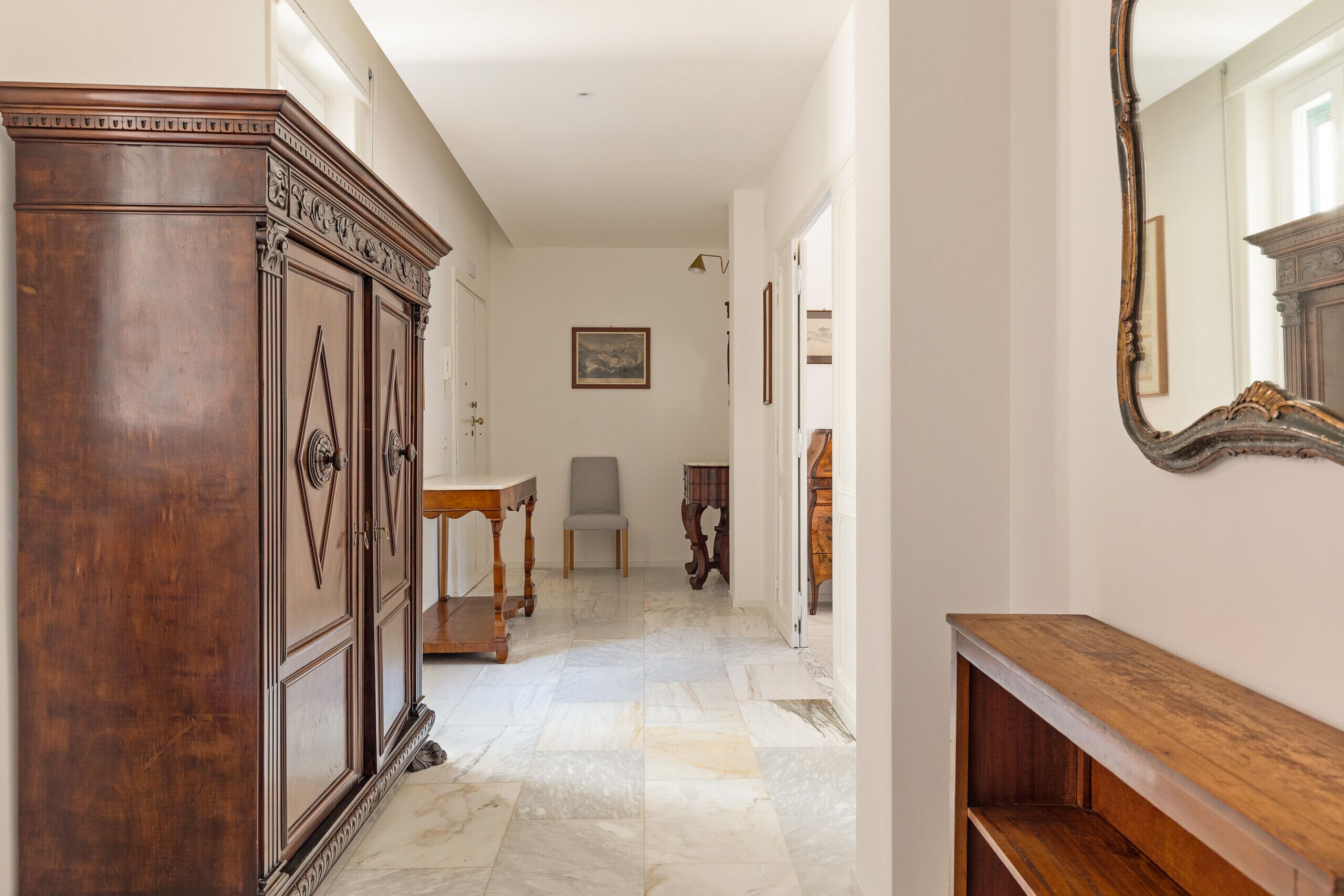 A hallway with a wooden cabinet, a marble floor, a wooden bench, and a mirror on the wall.