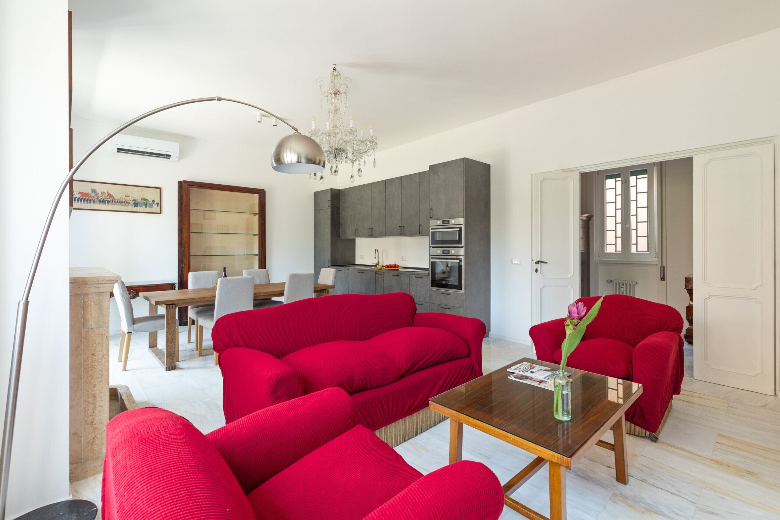 A modern living room with red sofas, a wooden coffee table, and a chandelier.