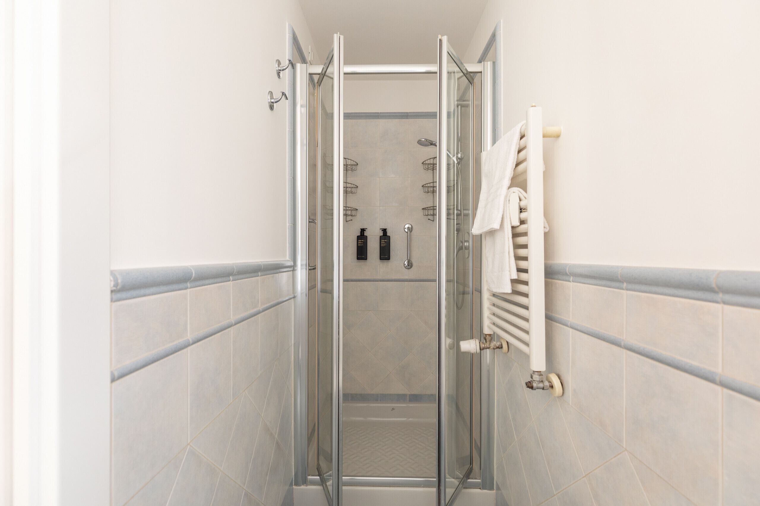 A glass-enclosed shower stall with a white towel rack and a white radiator on the wall.
