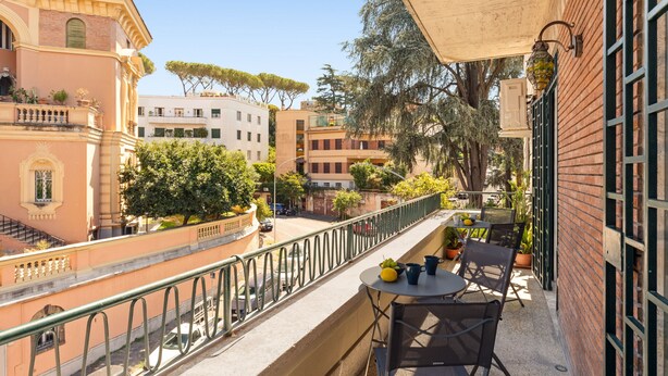 A balcony with a table and chairs, overlooking a street with buildings and trees. - Bright and Spacious 5BR Apartment in Pariol (Roma)