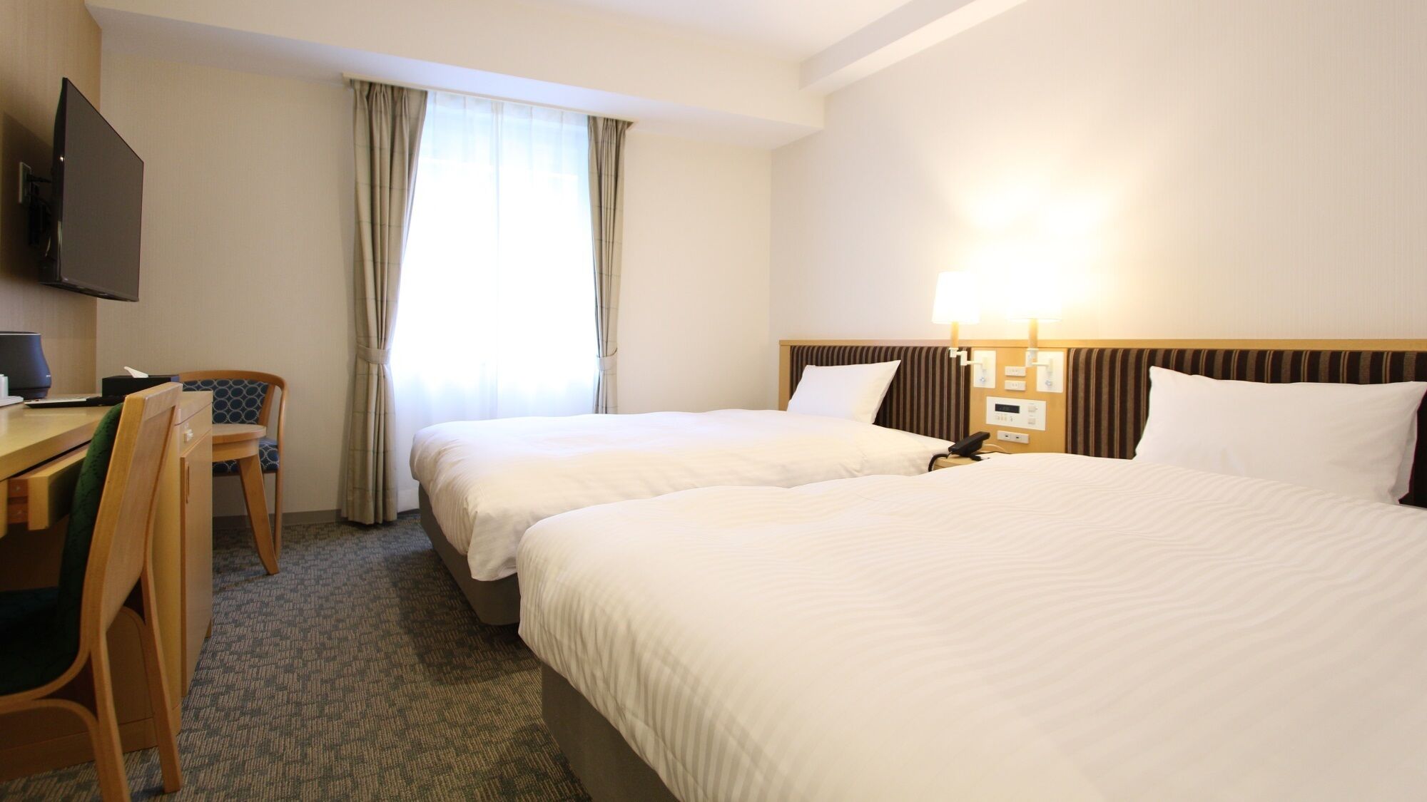 Een hotelkamer met twee bedden, een bureau met stoel, een televisie en een raam met gordijnen.
