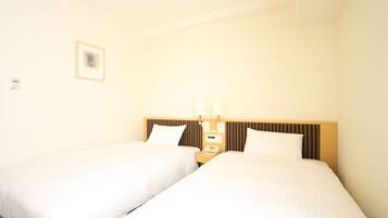 A hotel room with two single beds, a wooden headboard, a nightstand with a phone and a lamp, and a small framed picture on the wall.