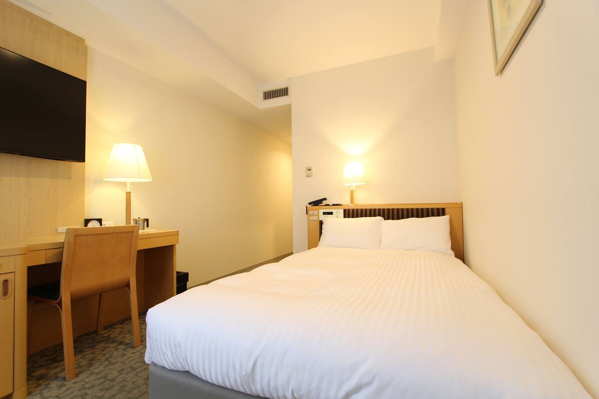 Een hotelkamer met een bed, bureau, stoel en twee bedlampjes.