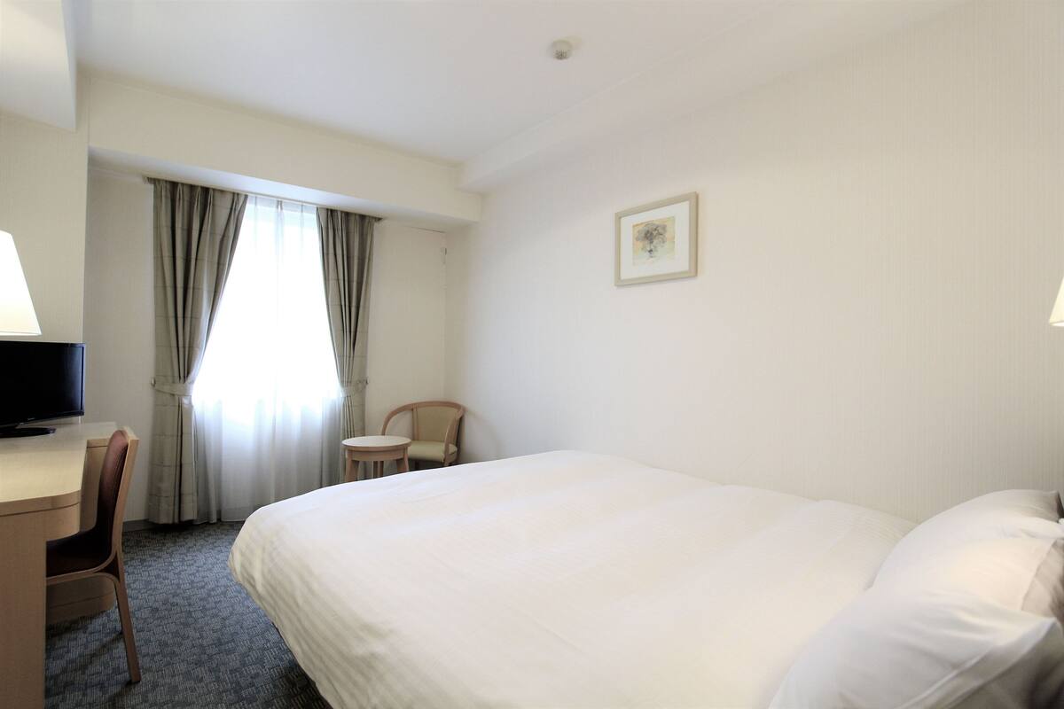 Een hotelkamer met een groot bed, een bureau met stoel, een televisie en een bijzettafeltje.