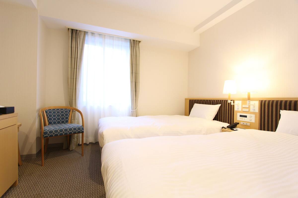Een hotelkamer met twee bedden, een bureau, een stoel en een lamp.