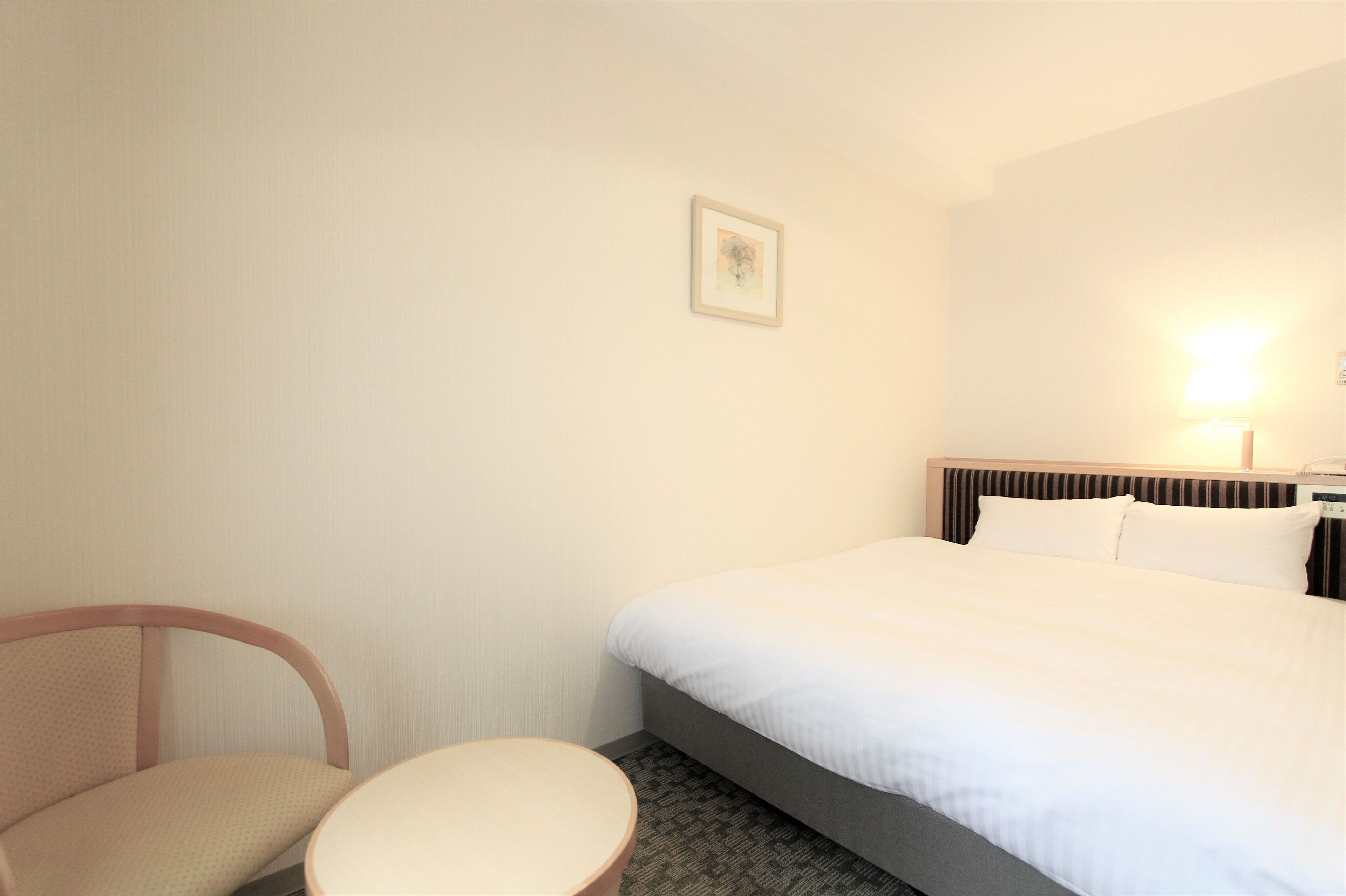 A hotel room with a bed, a chair, a small table, and a wall-mounted picture.