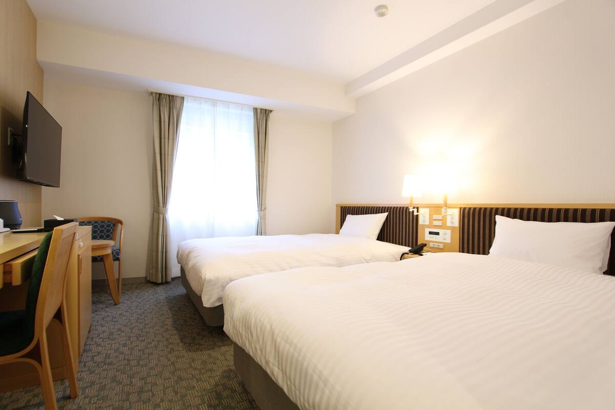 Hotelkamer met twee bedden, een bureau, een stoel, een televisie en een raam met gordijnen.