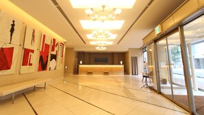 A hotel lobby with a reception desk, artwork on the walls, a bench, and a large chandelier. - KOKO HOTEL Sendai Station South (Sendai)