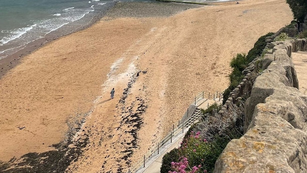 Ein Strand mit einer Steinmauer und freiem Blick auf das Meer.